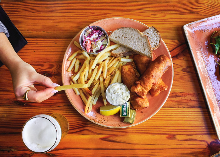 A hand grabbing a frite off of a coral-colored plate with Café Benelux's Classic Fish Fry